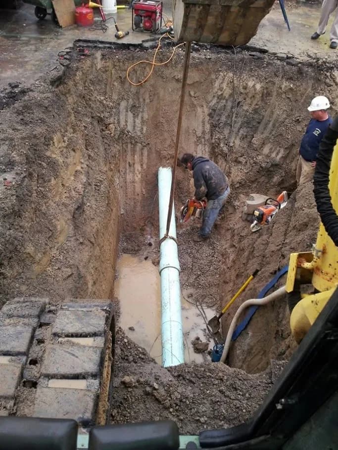 Brady crew cutting and setting large-diameter sewer pipe in a deep excavation