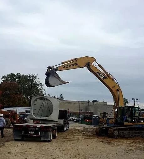 Brady excavator lifting a precast concrete vault for underground utility installation
